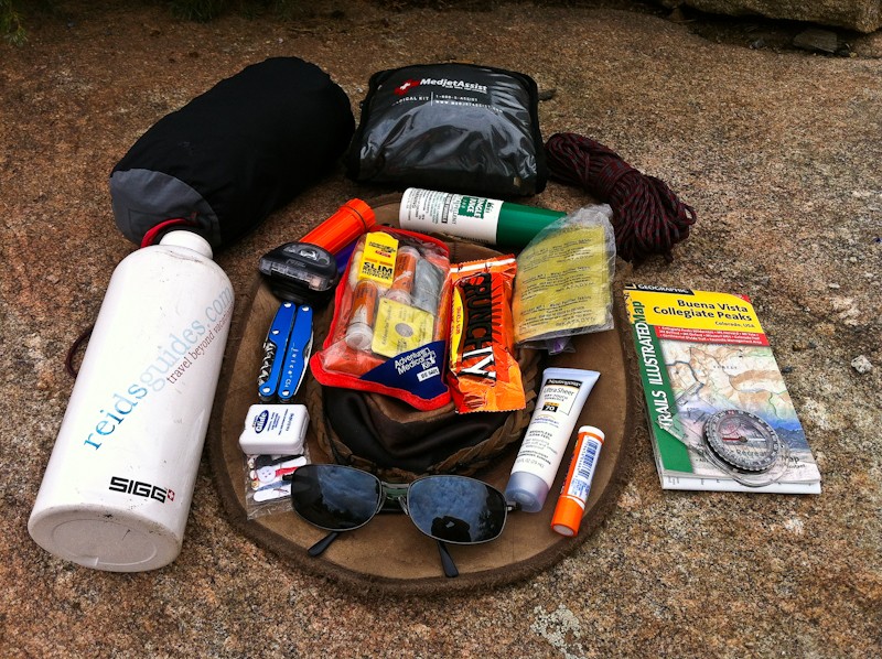 Gear laid out for the 10 essentials: water bottle, map and compass, first aid kit, tools, food, sun protection, and more